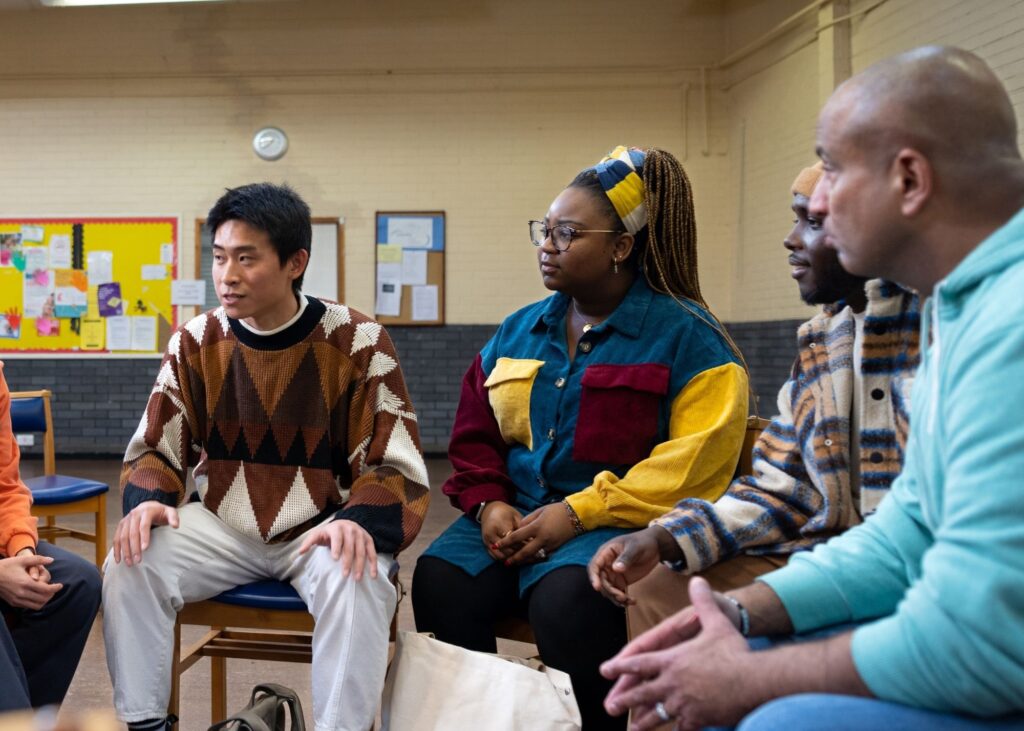 A small group of people sit in a circle talking, listening closely to one another during a community conversation.