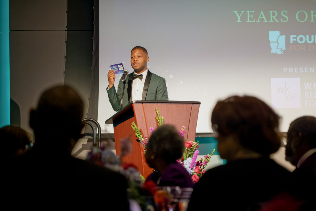 Greg Johnson stands at the podium holding a donation card during the 35th Anniversary celebration.
