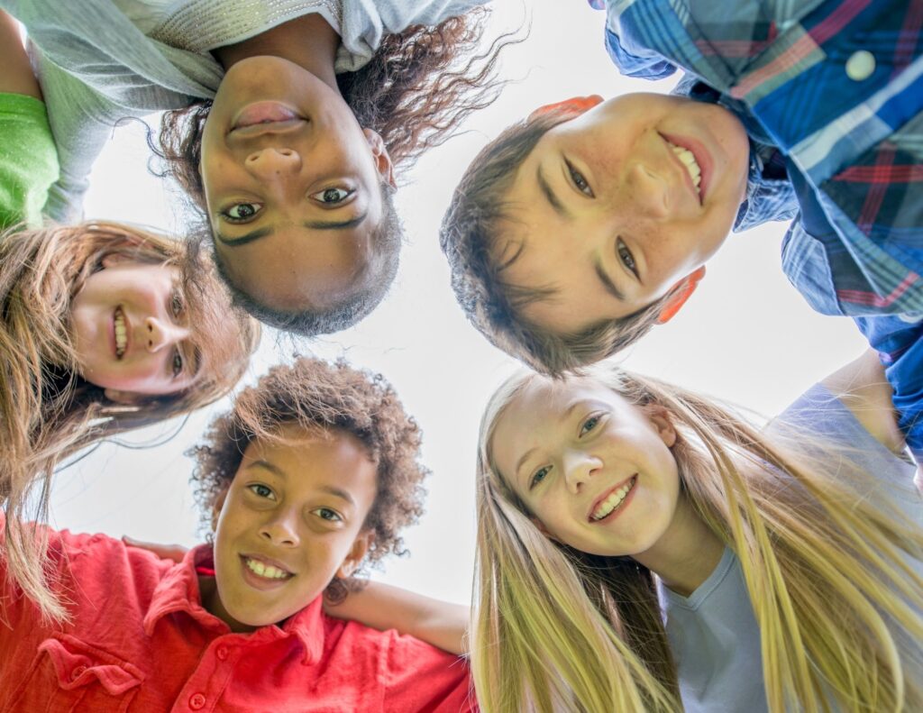 A diverse group of middle school students smiling as they stand in a circle and look down toward the camera.